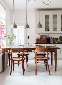 a dining room table and chairs in front of a window with hanging lights above it