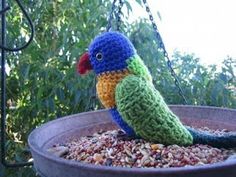 a crocheted bird sitting on top of a metal bowl filled with gravel and nuts