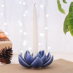 a white candle sitting on top of a wooden table next to a blue flower and pine cone