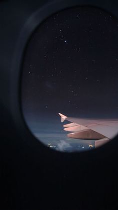 an airplane wing seen through the window of another plane at night with stars in the sky