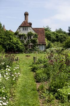 an old house in the middle of a field with lots of flowers and trees around it