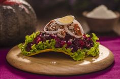 a wooden plate topped with lettuce and other food on top of a purple table cloth