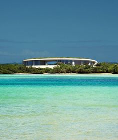 a house on an island in the middle of the ocean with trees and bushes around it