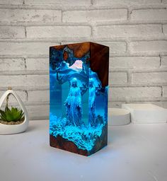 a wooden block with a statue in the middle and blue water on it next to a succulent plant