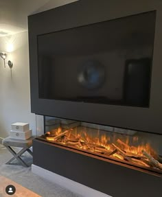 a living room with a large television and fire in the fireplace, next to a chair