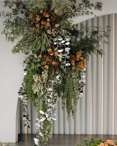 an arrangement of flowers and greenery hanging from the ceiling in front of a white wall