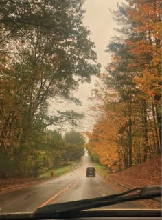 a car driving down a road surrounded by trees in the fall time with leaves on the ground