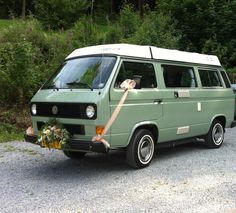 an old van with flowers tied to the front is parked in a gravel parking lot