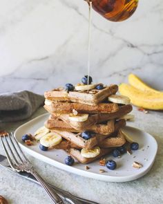 a white plate topped with waffles covered in blueberries and bananas next to syrup