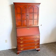 an old wooden desk with two drawers and a cupboard on top, against a white wall