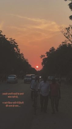 three people are walking down the road with their bikes and cars in the background as the sun sets