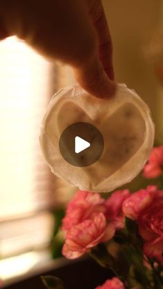 a person is holding a piece of wax paper over some pink flowers in front of a window