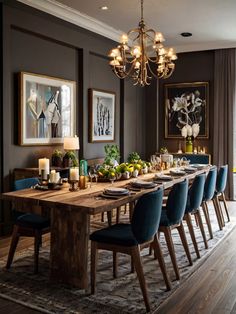 a dining room table with blue chairs and pictures on the wall behind it in front of a chandelier