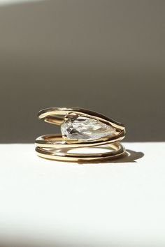 a gold ring with a pear shaped diamond on it's side, sitting on top of a white surface