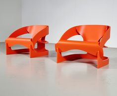 two orange chairs sitting next to each other on top of a white floor in front of a wall