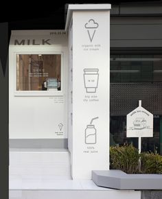 a white sign sitting on the side of a building next to a planter filled with flowers