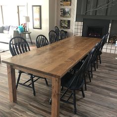 a large wooden table surrounded by black chairs in a room with wood floors and a fireplace