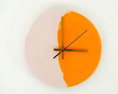 an orange and white clock with black hands on a wall in front of a white background