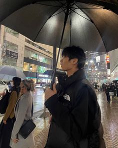 a man standing under an umbrella in the rain on a city street while people walk by