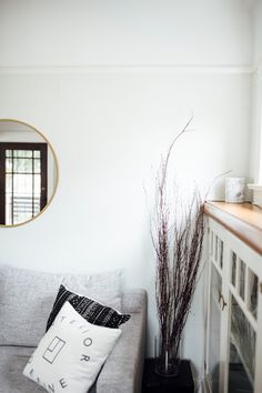 a living room with a couch, mirror and vase filled with flowers on top of it