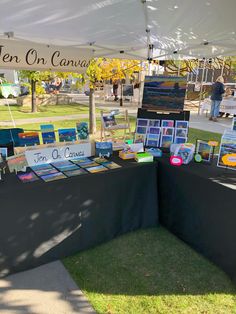 a table with paintings on it under a tent at an outdoor art show in the park