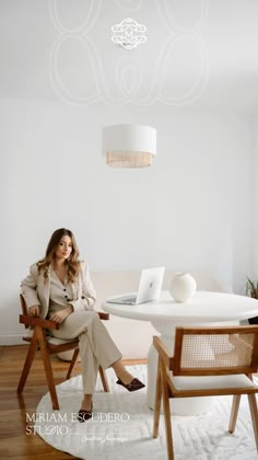 a woman sitting at a white table in front of a laptop on top of a wooden chair