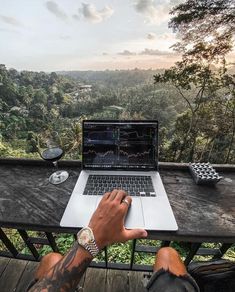 a man sitting at a table with a laptop computer on his lap looking out over the jungle