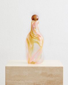 a small glass vase sitting on top of a wooden block in front of a white wall