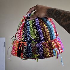 a hand holding a multicolored crocheted bag with string attached to it