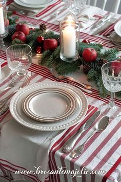 the table is set for christmas dinner with silverware, candles and red striped napkins