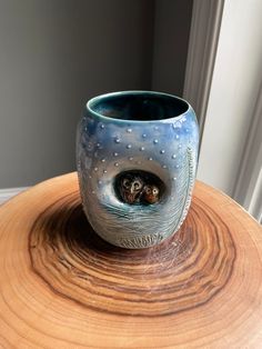 an owl is peeking out from its nest in a vase on top of a wooden table