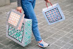 a woman carrying two shopping bags on the street with her legs crossed and one hand holding another bag