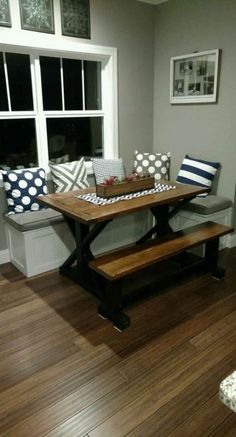 a wooden table sitting in front of a window next to a bench with pillows on it