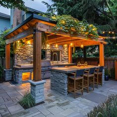 an outdoor kitchen is lit up at night with string lights on the roof and grill