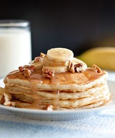 a stack of pancakes topped with bananas and nuts on a plate next to a glass of milk