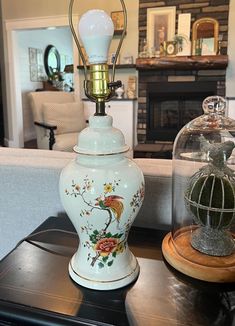 a lamp sitting on top of a table next to a glass dome with a bird in it