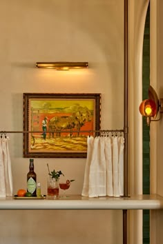 a painting hangs on the wall above a shelf with wine bottles and other items in front of it