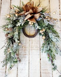 a wreath with pine cones and berries hanging on a wooden door, decorated with an ornament