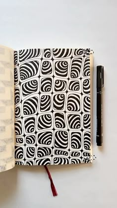 an open notebook with black and white designs on it, next to a fountain pen