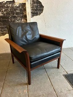 a black leather chair sitting on top of a tile floor next to a brick wall