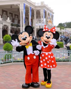 two mickey and minnie mouse characters standing in front of a building