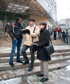 two men are standing on the steps in front of a building and one man is holding a book