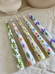 four candles with flowers painted on them are lined up in a row next to a vase