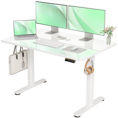 two computer screens sitting on top of a white desk next to a bag and purse