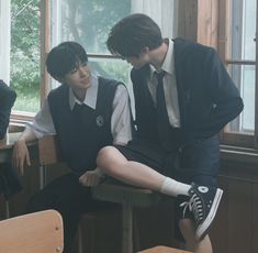 two young men sitting at desks in school uniforms