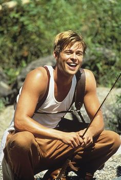 a man squatting down with a fishing pole in his hand and smiling at the camera