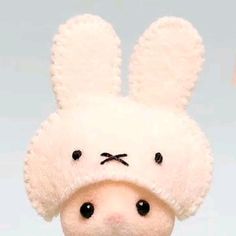 a white stuffed animal with black eyes wearing a bunny ears hat on top of it's head