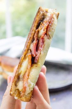 a person holding up a sandwich with bacon and cheese on it in front of a plate