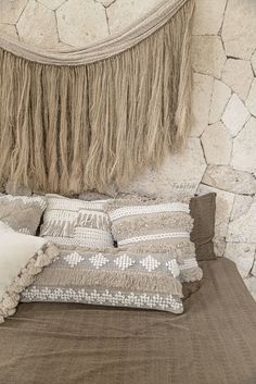 a bed topped with lots of pillows next to a wall covered in stone walls and fringes