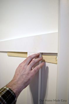 a hand is holding the edge of a piece of wood near a door handle on a white wall